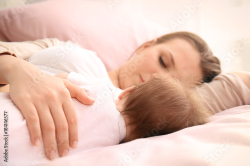 Young mother and cute baby sleeping on bed at home