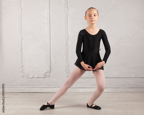 Young beautiful child girl ballerina standing practicing ballet wearing black tutu dress posing in studio with light gray antique cement background. Copy space image.