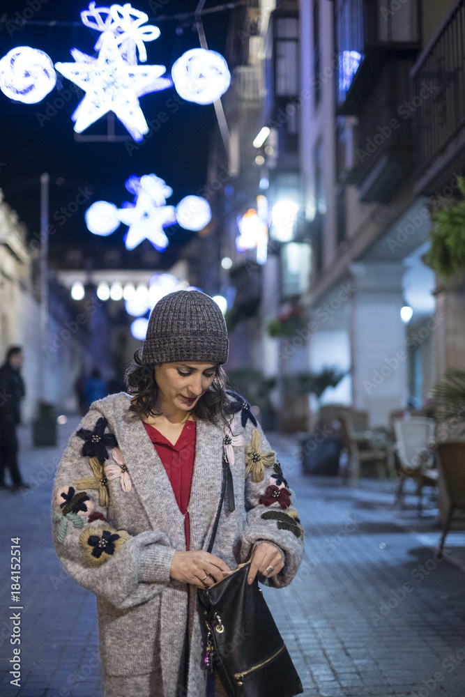 Woman looking for something at her hand bag while walking in the street in night holidays scene