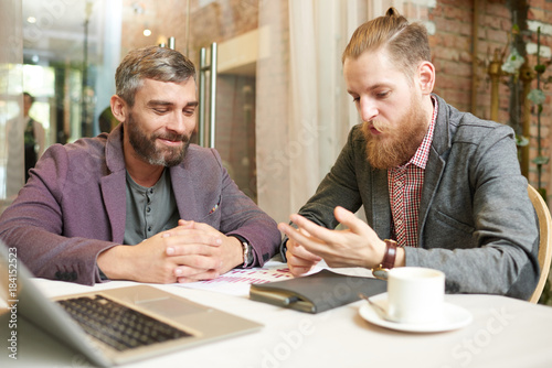 Portrait of two successful business men discussing work and using laptop during meeting in cafe on coffee break