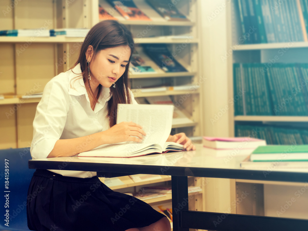 Asian Student in the Library of University. Young student concentrating to read a book against Blur Bookshelf, Education Asian Student in the Library of University. Young student concentrating to read a book against Blur Bookshelf, Education
