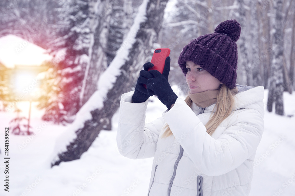girl in a winter forest with a fashionable modern mobile phone (smartphone) in special gloves for working with a touch screen