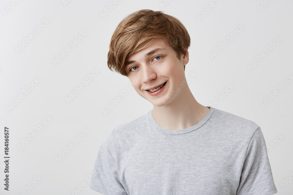 Friendly looking positive fair-haired young stylish man with blue eyes smiling broadly dressed casually, rejoicing his life, standing against gray studio wall. Youth, positive emotions and feelings Friendly looking positive fair-haired young stylish man with blue eyes smiling broadly dressed casually, rejoicing his life, standing against gray studio wall. Youth, positive emotions and feelings