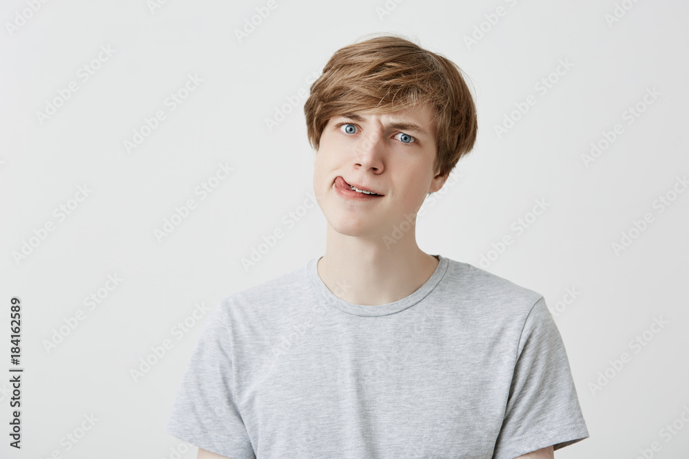 Surprised fair-haired guy dressed casually looks confused, shocked, and puzzled, thinks about something strange, thinks, makes hard decision. Human emotions, feelings and face expression.