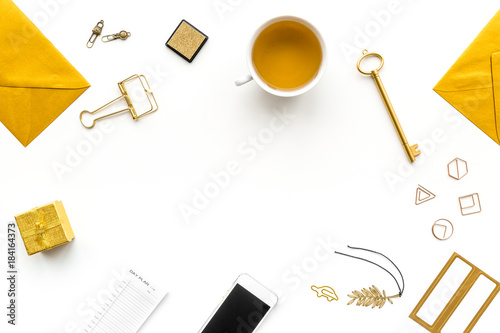 Office desk in trendy gold color. Glittering stationery near cup of tea, cell phone   on white background top view copyspace