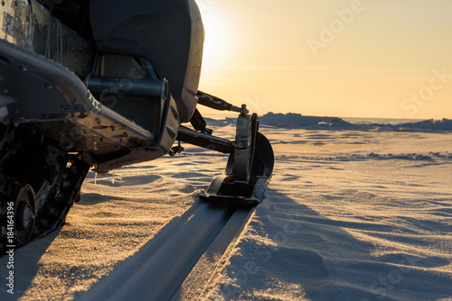 A snowmobile stands on the snow at sunset. photo