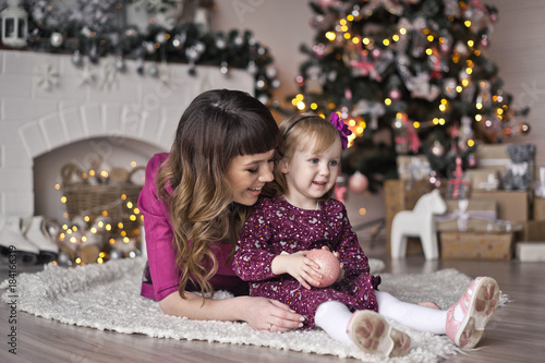 The child with the mother sitting on a white Mat around the Christmas tre