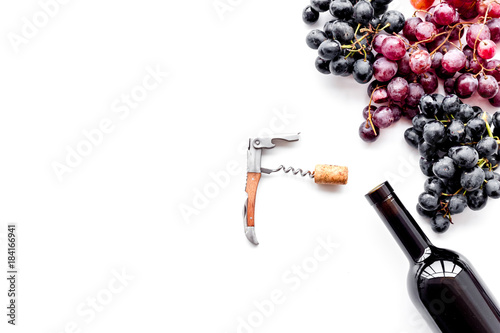Uncorking the wine bottle. Bottle, corkscrew and bunches of red and black grapes on white background top view copyspace