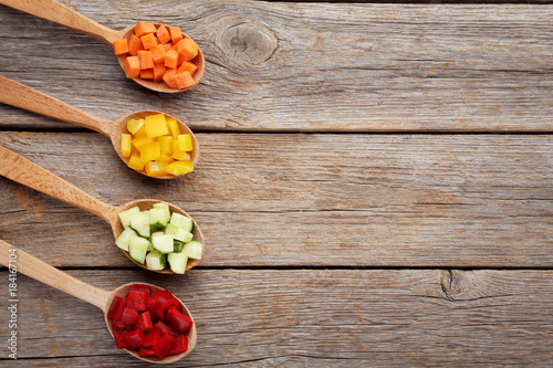 Fresh sliced vegetables in spoons on wooden table