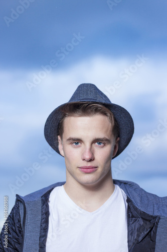 Fashion portrait of young man wearing hat with blue sky on the background.