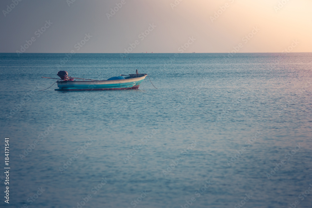 Fototapeta premium Beautiful seascape view of fishing boat floating on the sea with sunset light in the background. (Selective focus)