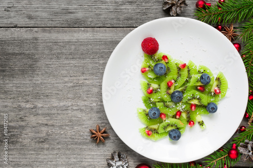 kiwi christmas tree with berries, pomegranate seeds and coconut looks like snow. funny food idea for kids photo