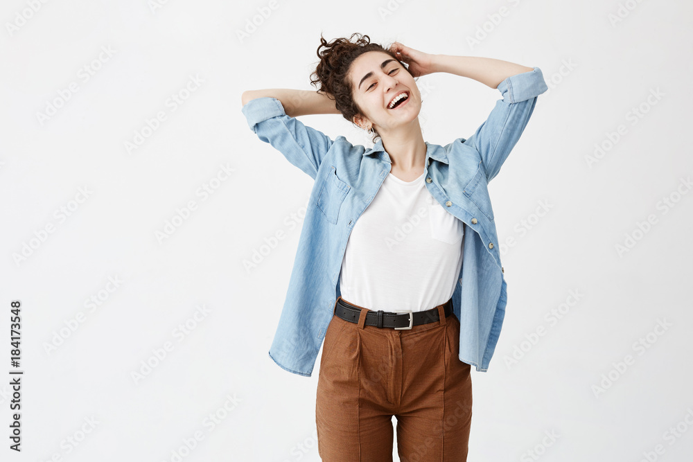 Playful young female with dark hair in bun wearing denim shirt with rolled up sleeves laughing at good joke, her look and expression full of joy and happiness. People and lifestyle concept Playful young female with dark hair in bun wearing denim shirt with rolled up sleeves laughing at good joke, her look and expression full of joy and happiness. People and lifestyle concept