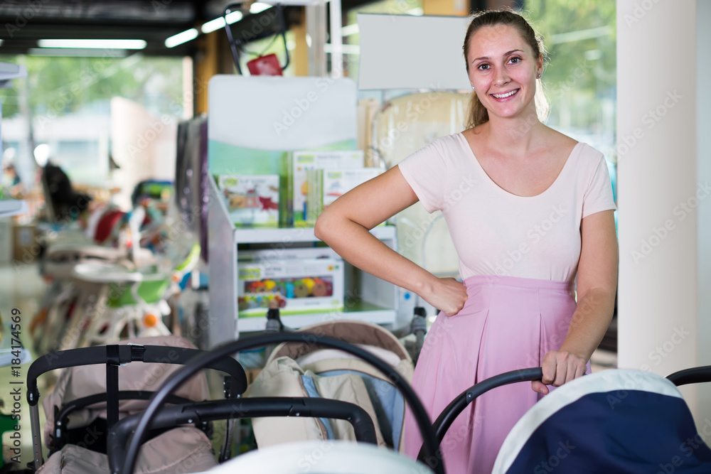 Young pregnant woman looking for baby carriage at kids shop