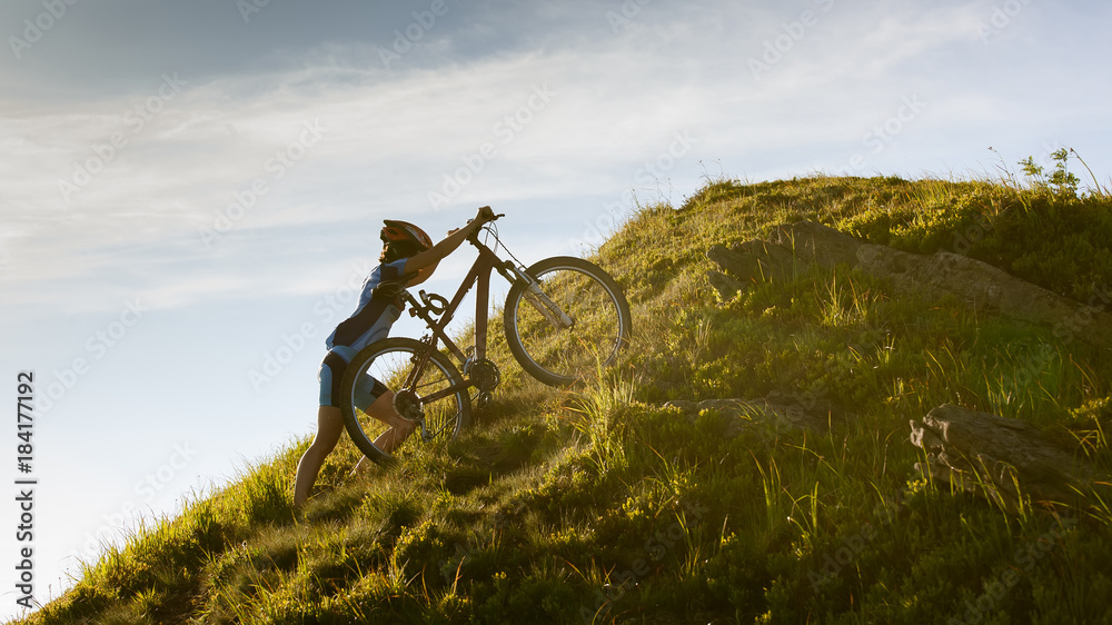 Obraz premium Biker pushes bicycle up in the mountains