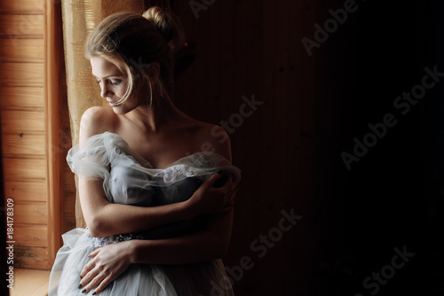 Beautiful girl with grey wedding dress and naked shoulders on the soft daylight from window