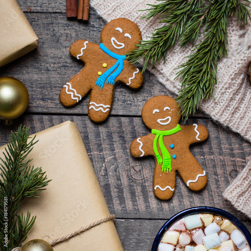 Christmas gift with gingerbread cookies and Cup of hot cacao with marshmallow, knitted blanket, pine cones, fir branches and toy tree on wooden rustic table background. Flat lay, top view, copy space photo