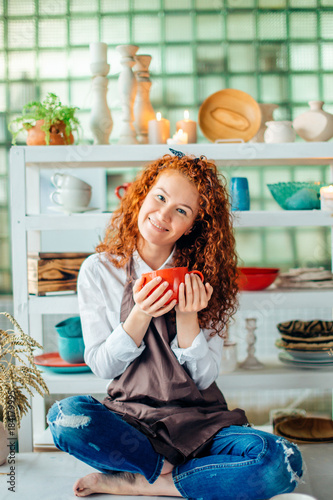 Beautiful redhead woman sitting in lotus pose in clay shop photo