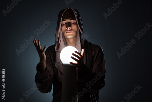 Photo Young wizard with crystal ball in dark room