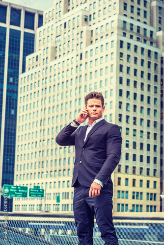 American businessman traveling, working in New York. Dressing in black suit, a young, strong, sexy professional standing in business district, listening, talking on mobile phone. .