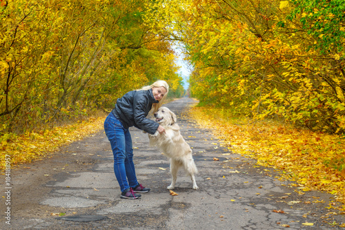 Young girl playing with dog golden retriver on the road in yellow forest. friendship with pets