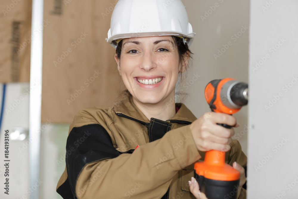 happy female builder in helmet with drill in hands smiling happy female builder in helmet with drill in hands smiling