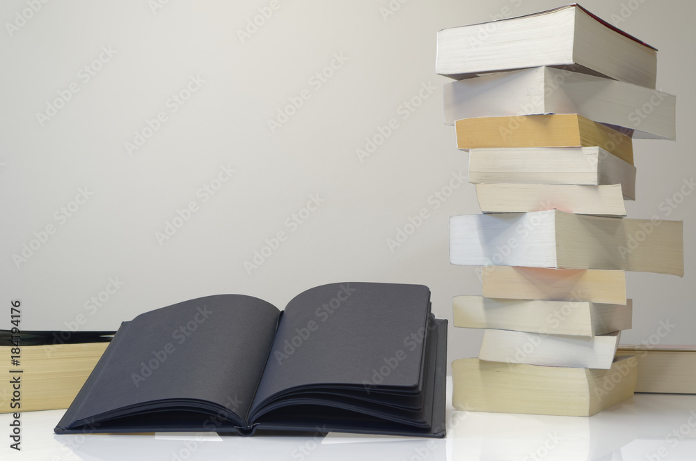 Black open book in foreground of pile of books Black open book in foreground of pile of books