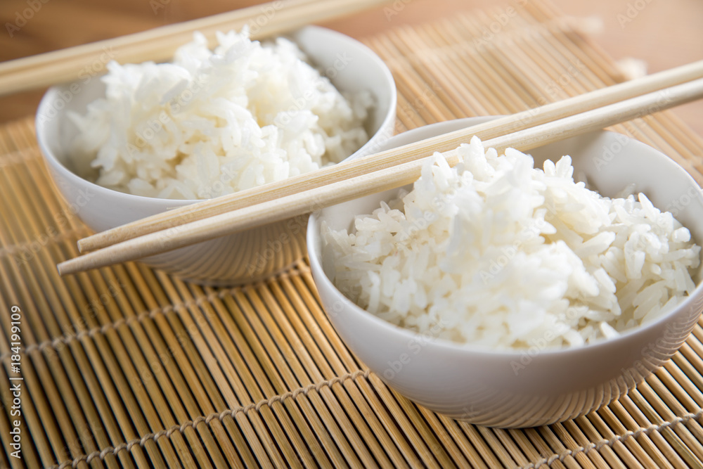 Zwei Schalen Basmati Reis mit Stäbchen auf Matte Zwei Schalen Basmati Reis mit Stäbchen auf Matte
