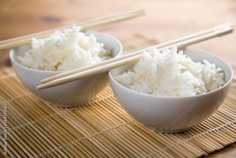 Zwei Schalen Basmati Reis mit Stäbchen auf Matte Zwei Schalen Basmati Reis mit Stäbchen auf Matte