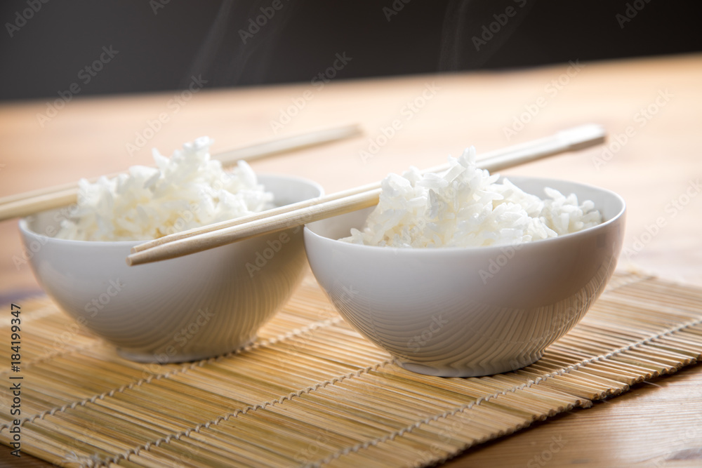 Zwei Schalen Basmati Reis mit Stäbchen auf Matte Zwei Schalen Basmati Reis mit Stäbchen auf Matte