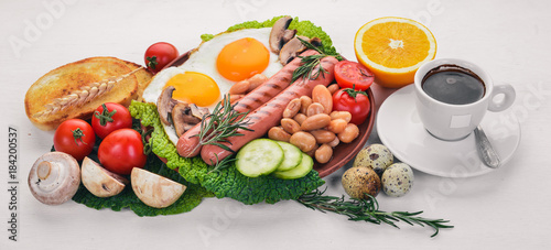 English breakfast tomatoes, sausages, beans, mushrooms, eggs,toast and herbs top view. On a white wooden background.