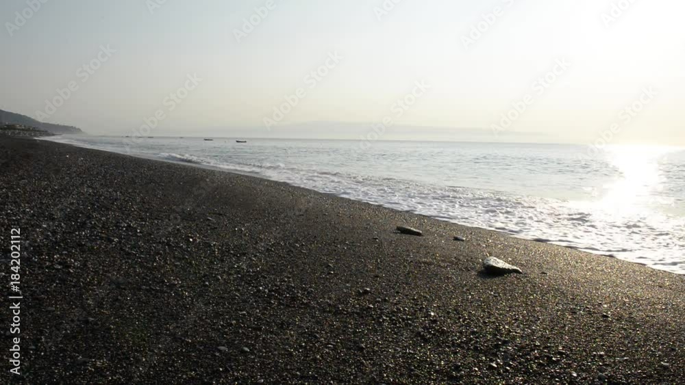 Onde del mare investono sassi sulla spiaggia nelle prime lucu della giornata una estiva Onde del mare investono sassi sulla spiaggia nelle prime lucu della giornata una estiva