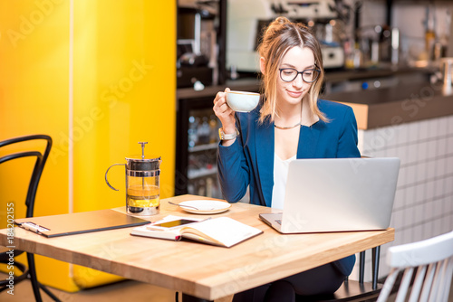 Young businesswoman strictly dressed in the suit working with laptop at the modern cafe interior