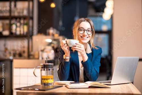 Young businesswoman strictly dressed in the suit drinking tea during the break at the modern cafe interior © rh2010