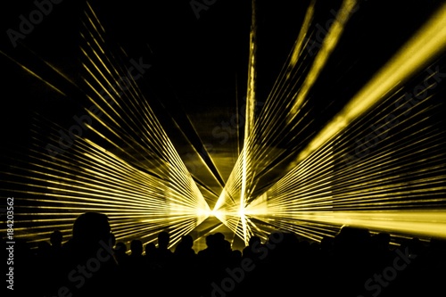 Yellow laser show nightlife club stage with party people crowd. Luxury entertainment with audience silhouettes in nightclub event, festival or New Year's Eve. Beams and rays shining colorful lights