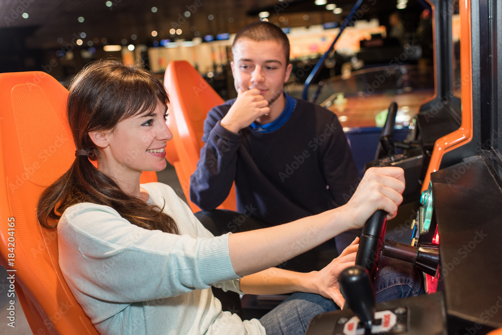 couple playing driving wheel video game in game room