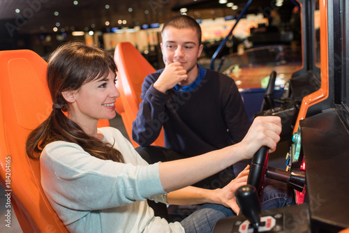 couple playing driving wheel video game in game room
