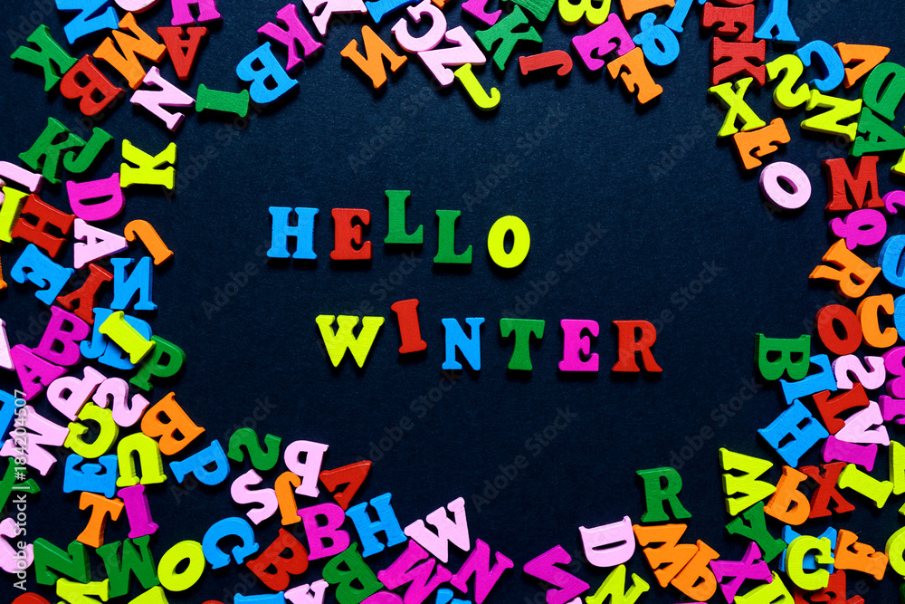 concept design - the word HELLO WINTER from multi-colored wooden letters on a black background, creative idea