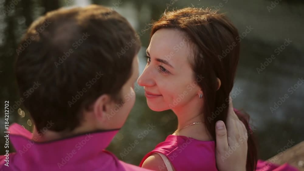 A beautiful girl and a guy are sitting by the river at sunset. Date of a loving couple outdoors
