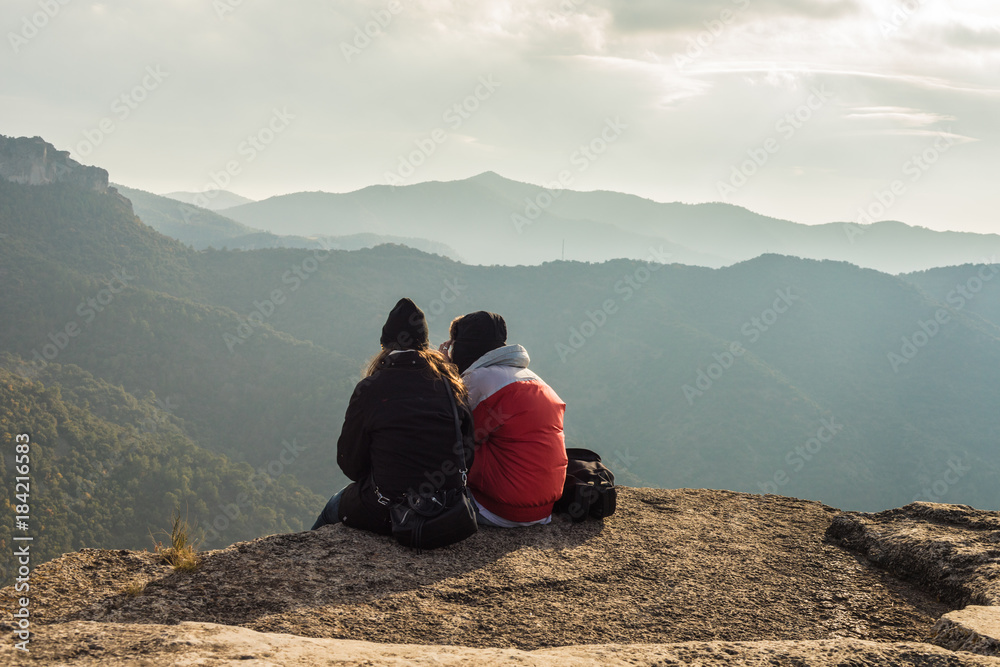 Couple sitting on high mountain peak watching the beautiful and surreal wilderness landscape in front of you in Siurana