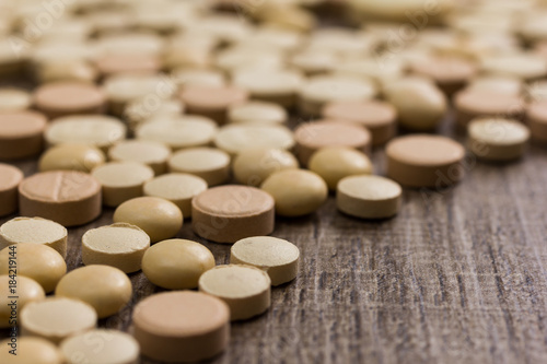 Heap of assorted beige capsules on wooden table.