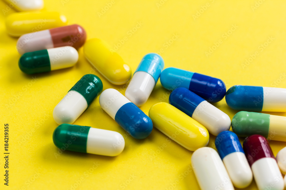 Heap of assorted colorful capsules on yellow table.
