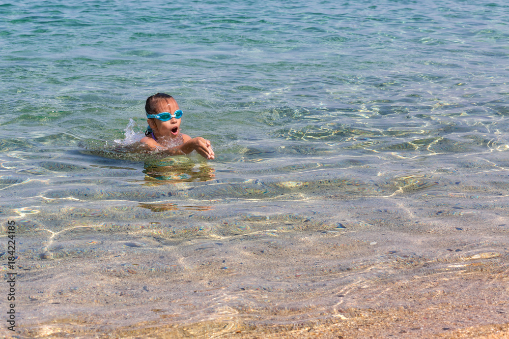 Young tourist girl in swimming sports glasses is floating in the Aegean Sea on the coast of Sithonia Peninsula