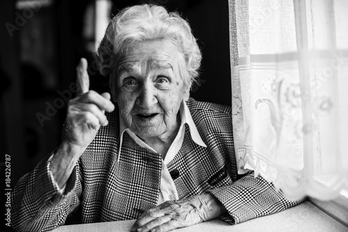 Elderly lady speaks sitting at the table. Black and white portrait.