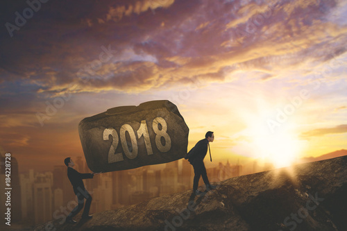 Business people lifting number 2018 on the cliff