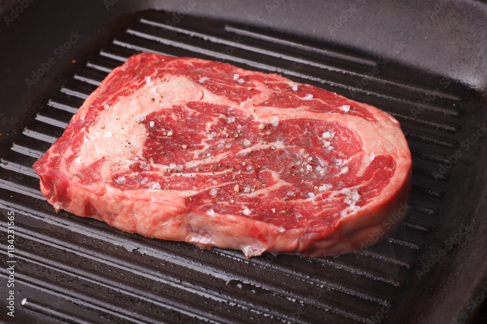 raw marble beef stake seasoning with salt and pepper - ribeye on grill pan raw marble beef stake seasoning with salt and pepper - ribeye on grill pan