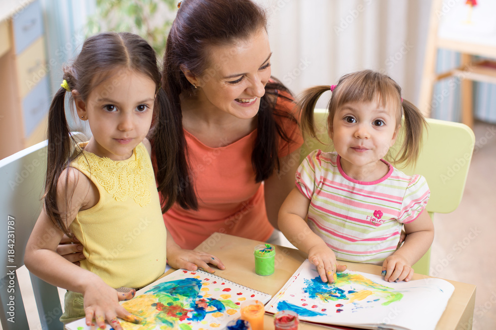 Fototapeta premium Mother and daughters are painting together. Happy family are coloring with paintbrush. Woman and children have a fun pastime.