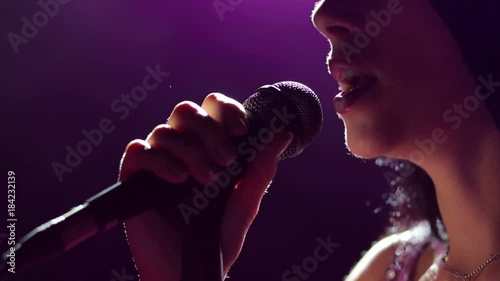 Close-up of the face of the singer with microphone on a black smoky background. The singer sings a song on stage in the dark, smoke, purple light, concert.