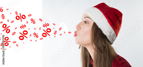 portrait of young christmas woman wearing red santa claus hat blows discount percentages text isolated on white background, copy space photo