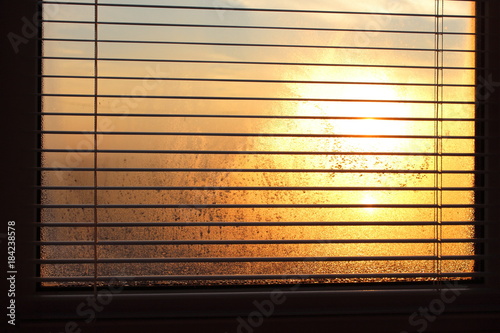 A misted window with metal jalousie in the early morning.